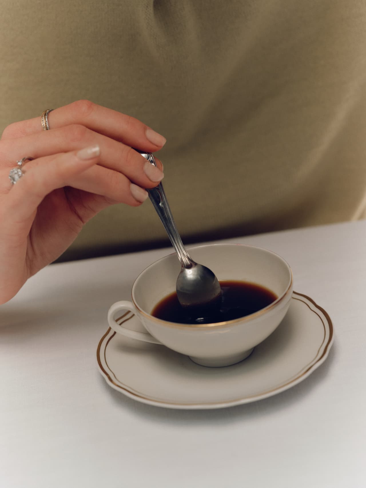 A hand stirring coffee in a gold-rimmed cup