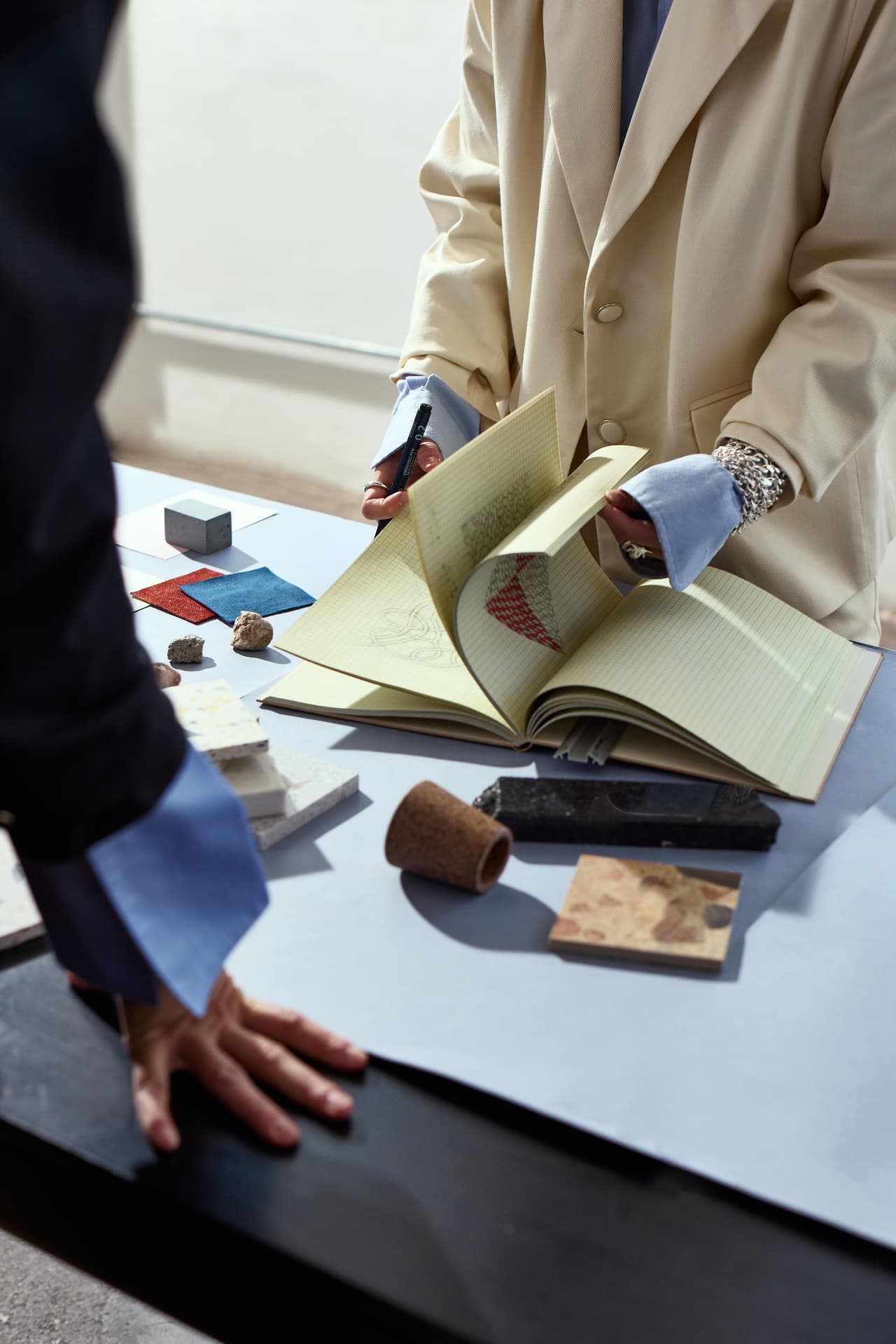 Hands writing in a ledger notebook at a sunlit desk